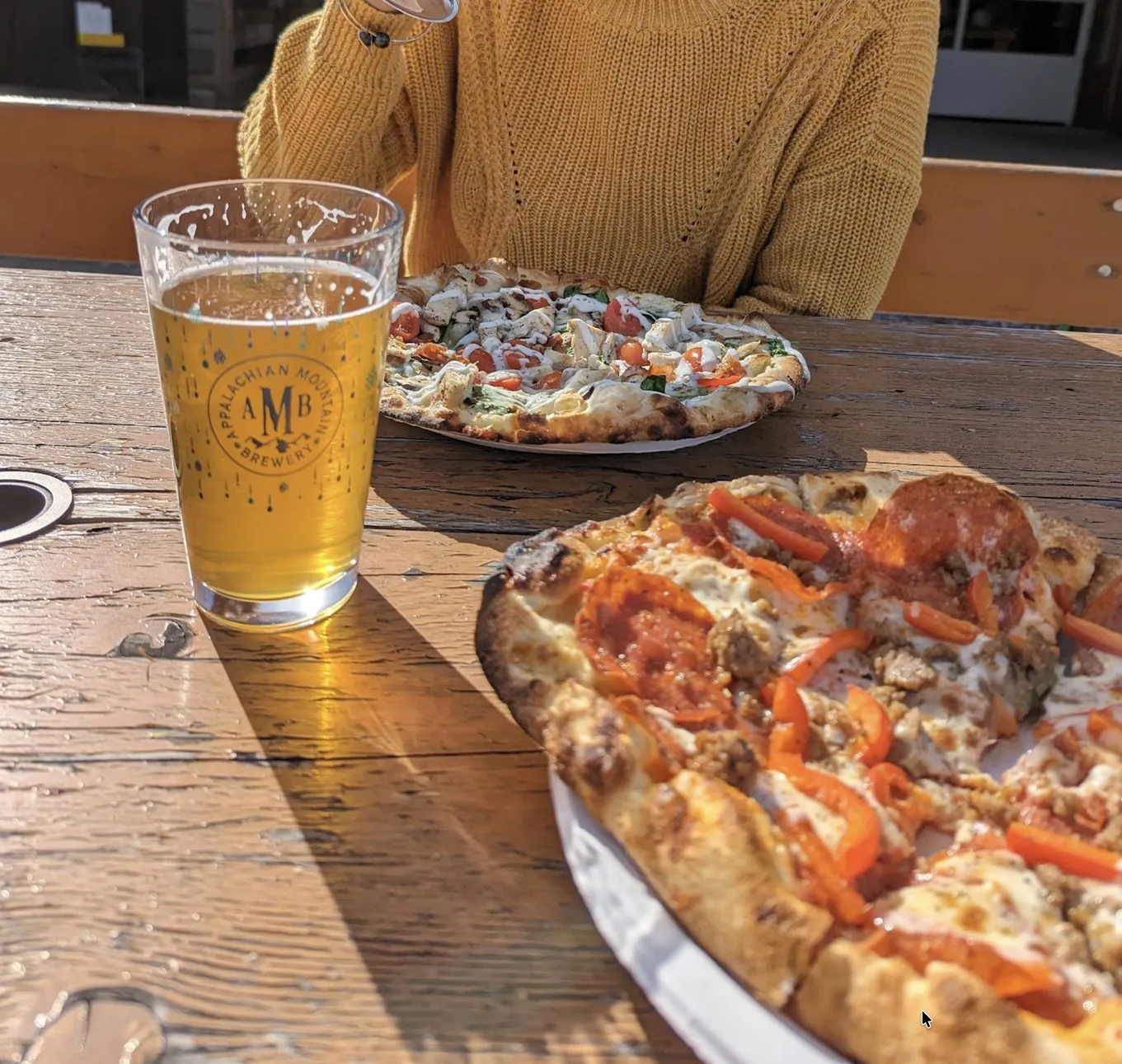 Two wood-fired pizzas and an AMB beer on a sunny patio table